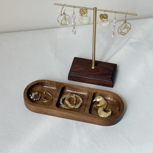 May include: A wooden jewelry organizer with a gold-toned earring display stand. The organizer has three compartments holding gold earrings and rings. The stand displays various dangling earrings with pearl and crystal accents.