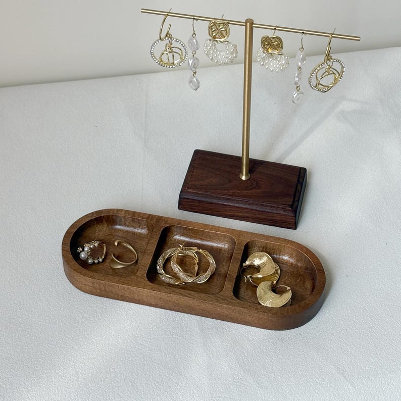 May include: A wooden jewelry organizer with a gold-toned earring display stand. The organizer has three compartments holding gold earrings and rings. The stand displays various dangling earrings with pearl and crystal accents.