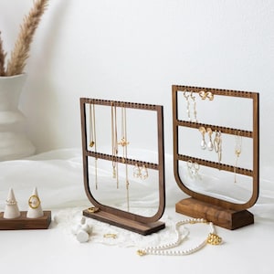 May include: Two wooden jewelry organizers with a dark brown finish. The organizers have a rectangular frame with multiple rows of holes for hanging necklaces and earrings. Various gold necklaces and earrings are displayed on the organizers.