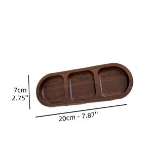 May include: A wooden serving tray with three compartments. The tray is oval-shaped and measures 20cm (7.87") long and 7cm (2.75") wide. The tray is made of dark brown wood.