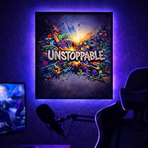 May include: A framed art print with the word "UNSTOPPABLE" in white, surrounded by a colorful graffiti-style design. The artwork is illuminated by a purple LED light, creating a vibrant and energetic atmosphere. The overall theme is motivational and artistic.