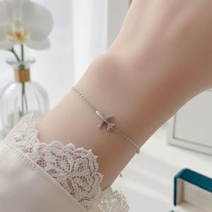 Può includere: Un braccialetto con ciondolo a forma di aereo argentato. Il braccialetto presenta una delicata catena con un piccolo ciondolo a forma di aereo adornato da accenti scintillanti. Un accessorio elegante.