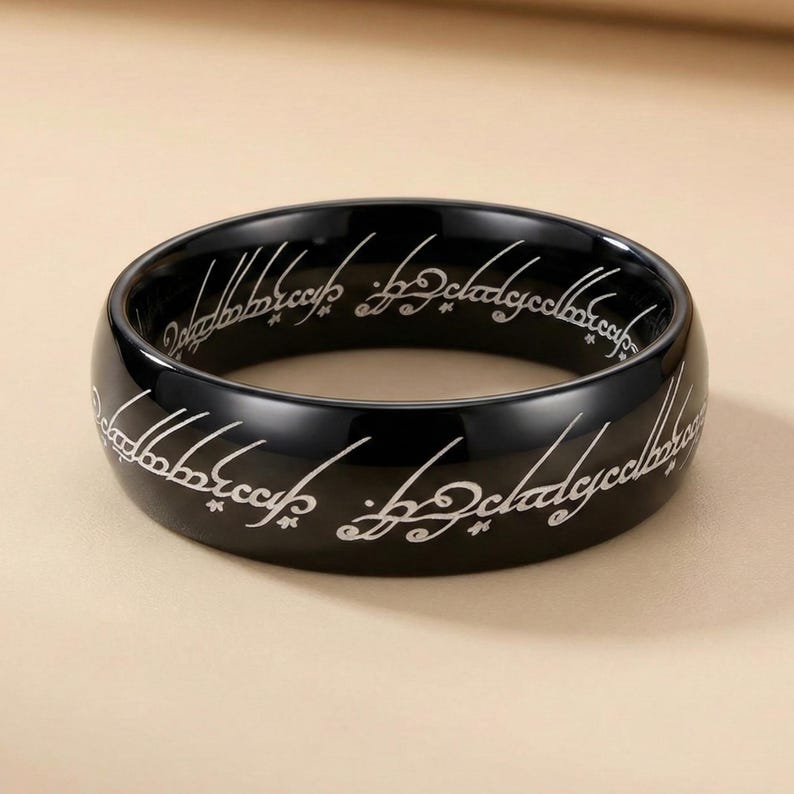 K&ouml;nnte beinhalten: Ein schwarzer Ring mit wei&szlig;er, eingravierter Schrift um das Band. Der Ring hat eine polierte, reflektierende Oberfl&auml;che. Die Schrift scheint in einer stilisierten Fantasiesprache zu sein. Der Ring ist ein massives Band mit glattem, abgerundetem Rand.