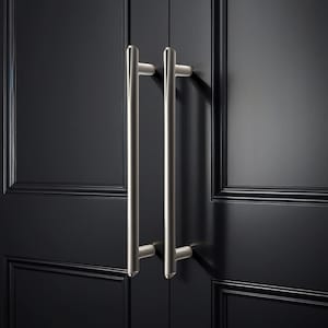 Może przedstawiać: Zbliżenie czarnych drzwi szafki z dwoma uchwytami drążkowymi ze szczotkowanego niklu. Uchwyty są ustawione pionowo i mają cylindryczną konstrukcję. Drzwi szafki mają wpuszczaną konstrukcję panelu z błyszczącym wykończeniem.