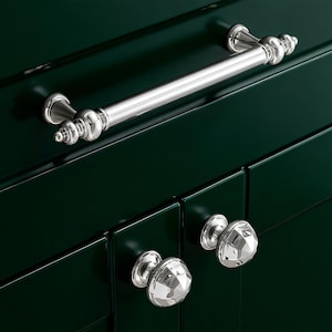 Pode incluir: Uma imagem em close-up de um armário verde escuro com ferragens prateadas. O armário apresenta uma longa barra horizontal e dois puxadores de cristal facetado. As ferragens brilhantes e reflexivas contrastam com a superfície verde escura.