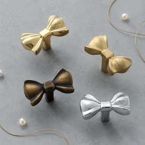 May include: Four bow-shaped cabinet knobs in polished gold, brushed gold, antique bronze, and polished chrome finishes. Each knob features an engraved circular design on the right side with the text Est 2026 R & Q surrounded by a decorative border.