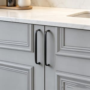 May include: Close-up of a light gray cabinet with two black, curved handles. The cabinet doors have a recessed panel design. A white countertop with a marble pattern is above the cabinet.