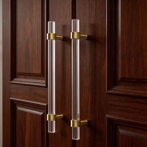 Könnte beinhalten: Zwei transparente Acryl-Schrankgriffe mit goldfarbenen Metallakzenten sind an einer dunkelbraunen Holzschranktür angebracht. Die Griffe sind zylindrisch und haben ein modernes, minimalistisches Design.
