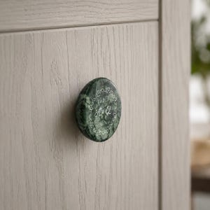 Op de afbeelding: Een ronde, donkergroene marmeren kastknop met een gepolijste afwerking, voorzien van een gegraveerde witte decoratieve rand, de letters K & Q en de tekst Est. 2020. De knop is bevestigd op een lichtbeige kastdeur met houtnerf.