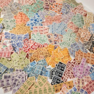 May include: A large collection of vintage postage stamps in various colors, including blue, green, orange, and pink. The stamps feature diverse designs and text, arranged in a scattered pattern. Some stamps have the text "D-D" and "GENIE".