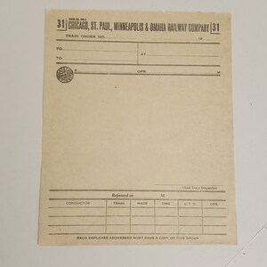 May include: A vintage train order form from the Chicago, St. Paul, Minneapolis & Omaha Railway Company. The cream-colored paper features printed text and lines for filling in details. The form includes the company name, train order number, and spaces for conductors and dispatchers.