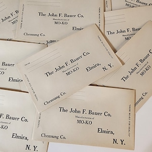 May include: A stack of vintage postcards advertising "MO-KO" a beverage. The postcards feature the company name "The John F. Bauer Co." and the slogan "Drink MO-KO for Health". The postcards are printed on cream-colored paper with black ink.