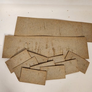 May include: A collection of brown cardboard pieces of various sizes and shapes. The pieces are arranged in a pile on a white surface.