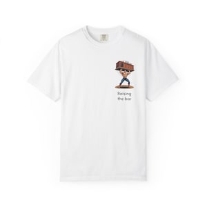 Op de afbeelding: Een wit T-shirt met korte mouwen en een afbeelding op de borst van een gespierd figuur die een houten bar boven het hoofd tilt. Onder de illustratie staat de tekst "Raising the bar" in een eenvoudig, donker, schreefloos lettertype.