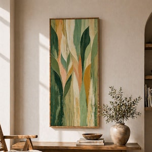 Puede incluir: Pintura abstracta enmarcada con pinceladas verticales en tonos verdes, amarillos y melocotón. Sobre un banco de madera con un jarrón y un cuenco. Una silla y una alfombra tejidas completan la habitación.