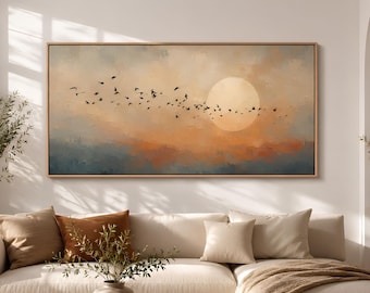 May include: A rectangular landscape painting in a light wood frame featuring a flock of birds flying across a hazy, warm-toned sky with a large, pale sun. The artwork displays soft gradients of orange, cream, and muted blue, creating a serene scene.