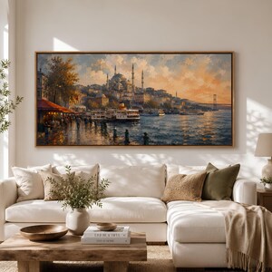 May include: A rectangular landscape painting in a wooden frame depicting a waterfront city scene with a mosque, minarets, and boats on the water at sunset. The sky is filled with warm orange and blue clouds, and the city architecture is illuminated.
