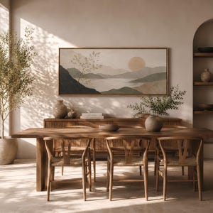 May include: A rectangular landscape painting in a wooden frame featuring a muted color palette of beige, green, and dark gray. The artwork depicts a serene mountain range, a calm body of water, and a large circular sun, creating a peaceful scene.