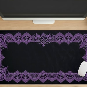 May include: Black rectangular mousepad with a purple lace design border featuring skulls, roses, and a crown. A white mouse rests on the pad. The mousepad is on a wooden desk with a computer monitor and a small cactus.