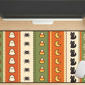 May include: A rectangular desk mat featuring vertical stripes with repeating Halloween icons including orange pumpkins, white ghosts, black spiders, candy corn, yellow crescent moons, black cats, and white spiderwebs on green, orange, and cream backgrounds.