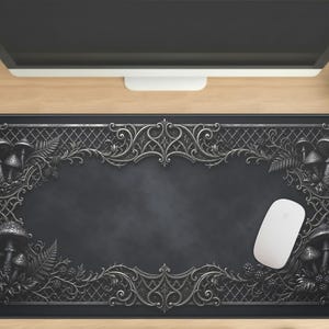 Puede incluir: Alfombrilla de escritorio rectangular negra con un borde plateado decorativo con setas, hojas y bayas. Un ratón de ordenador blanco descansa sobre la alfombrilla. La alfombrilla está diseñada para proteger la superficie del escritorio.