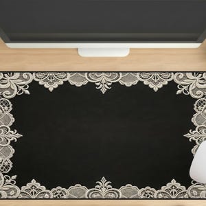 May include: A rectangular desk mat featuring a solid black center and a wide, intricate cream-colored lace border pattern that frames the entire perimeter. The mat has rounded corners and a smooth surface, with a white computer mouse resting on it.