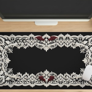 May include: Black rectangular mousepad with a white lace design border. The design includes a bat with a skull in the center. A white computer mouse is on the right side of the pad.