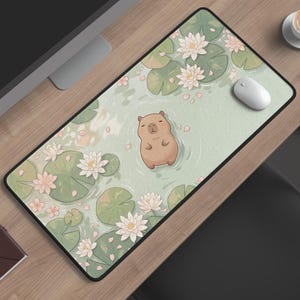 Op de afbeelding: Rechthoekige muismat met een grillige illustratie van een capibara die in een vijver met waterlelies en bloemen drijft. De mat heeft een zwarte rand en ligt op een houten bureau.