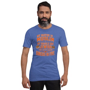Op de afbeelding: Een blauw gemêleerd t-shirt met korte mouwen en oranje tekst: MY MAYOR IS MUSLIM, MY BAGELS ARE JEWISH, THE CITY'S ALIVE, KNICKS IN FIVE. Twee kleine bagel-illustraties staan tussen het woord JEWISH en de tekst die eronder staat.