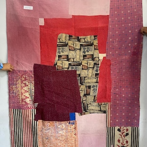 May include: A patchwork textile in shades of red, pink, and burgundy. The design incorporates various patterns, including stripes, polka dots, and floral motifs. The textile has a tag that reads "VQ1466".