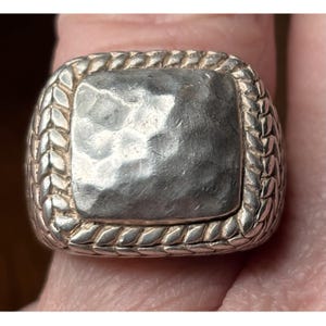 May include: Silver-toned ring with a hammered square center and a braided border. The ring is a statement piece, showcasing a textured design. The metal has a slightly aged appearance, adding to its vintage appeal. The ring is a bold accessory.