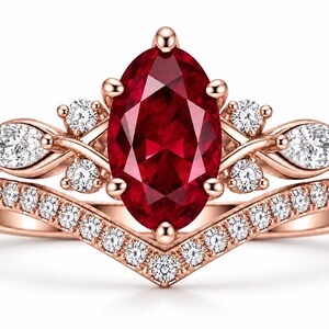 May include: A rose gold ring set featuring a central marquise-cut deep red gemstone. The band is accented with small round white stones and two pear-cut white stones on each side. A separate chevron-shaped band with pavé-set white stones sits below.