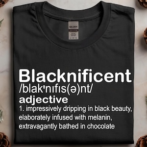 Peut inclure: T-shirt noir avec le mot "Blacknificent" en blanc et une définition. La définition comprend des phrases telles que "impressionnant de beauté noire" et "somptueusement baigné dans le chocolat."