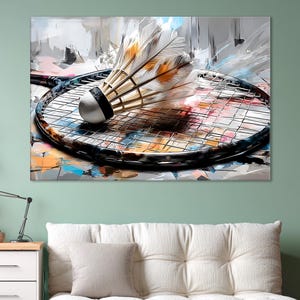 Puede incluir: Un volante de bádminton con plumas blancas y naranjas descansa sobre una raqueta de bádminton negra. La obra de arte presenta un fondo abstracto colorido con pinceladas grises, azules y naranjas.