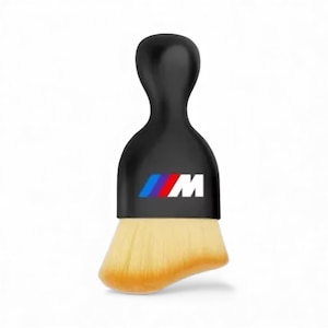 May include: A black makeup brush with a curved handle and a logo featuring blue, red, and white stripes with the letter "M". The brush head is a light tan color.