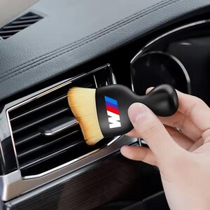 K&ouml;nnte beinhalten: Eine schwarze Autoreinigungsb&uuml;rste mit Griff und weichen, hellbraunen Borsten. Die B&uuml;rste zeigt das BMW-Logo in Rot, Blau und Wei&szlig;. Die B&uuml;rste wird zur Reinigung einer Autol&uuml;ftung verwendet.