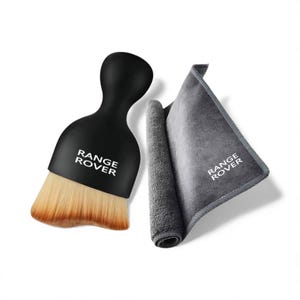 May include: A black brush with tan bristles and a grey microfiber cloth, both bearing the white "RANGE ROVER" logo. The brush has a rounded handle. The cloth is folded and rolled.