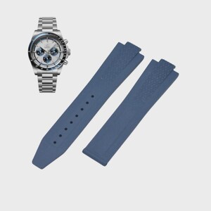 May include: A stainless steel chronograph watch with a white dial and blue sub-dials is displayed next to a pair of blue watch straps. The straps are made of a textured material and have a pin-and-buckle design.