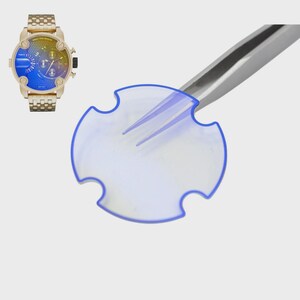 May include: A gold-toned wristwatch with a blue, yellow, and purple face and a matching gold band. A clear, circular watch component with a blue border is held by silver tweezers.