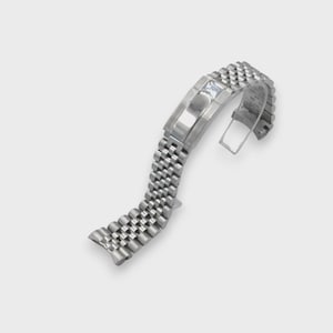 May include: A silver watch strap with a textured design. The strap is made up of small, interconnected links and features a rectangular clasp with a small, clear gem. The strap is curved, indicating flexibility and a design to fit a wrist.