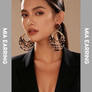 Puede incluir: Pendientes de aro grandes y en capas con un patrón de carey. Los pendientes tienen un marco de metal dorado y un pequeño perno redondo marrón. La imagen también incluye el texto "MIA EARRING".