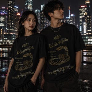 Könnte beinhalten: Zwei Personen tragen schwarze T-Shirts mit einer Schlangengrafik und dem Text "Filip Longhitano Specialized in Hognose" in Gold. Die Website-Adresse www.HETERODON.com ist ebenfalls auf den Shirts aufgedruckt. Der Hintergrund zeigt eine nächtliche Stadtlandschaft.