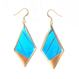 May include: A pair of gold earrings with blue butterfly wings encased in a diamond-shaped frame.