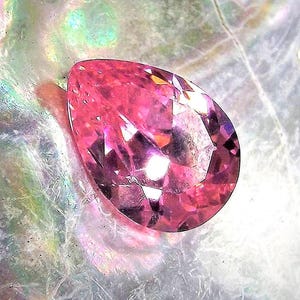 Pink pear cut faceted Cubic Zirconia angled to the left over abalone shell background