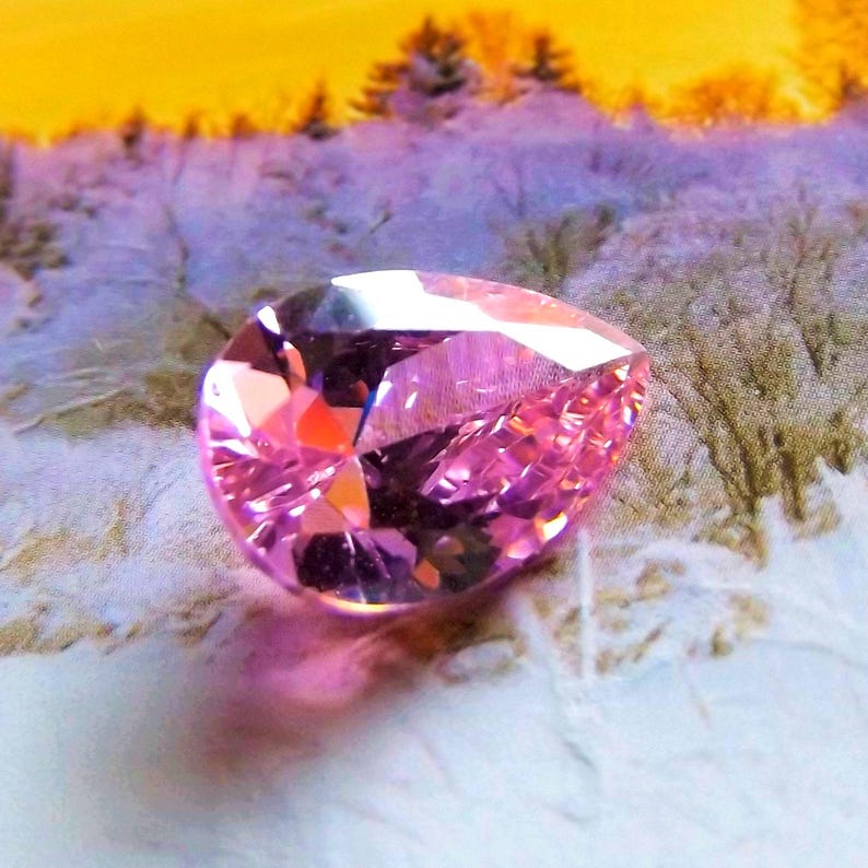 Pink pear cut 8x12mm CZ gem in a snowy setting, reflecting pink light and shadow