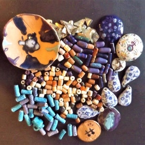 May include: A collection of colorful ceramic beads, pendants, and a small dish. The beads are in shades of blue, turquoise, brown, and white. The pendants are in various shapes and sizes, including teardrop, round, and square. The dish is a small, round, ceramic dish with a blue and brown glaze.