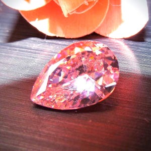 Pink teardrop shaped faceted CZ gem stone with pink rose pedals in the background