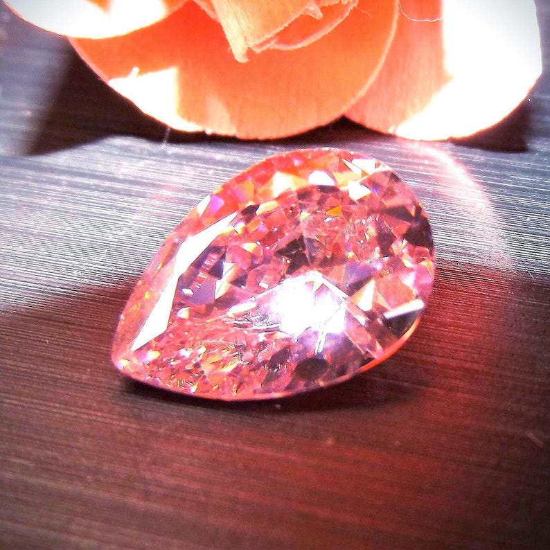 Pink teardrop shaped faceted CZ gem stone with pink rose pedals in the background