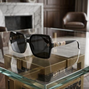 Puede incluir: Gafas de sol cuadradas negras con lentes oscuras. Las gafas de sol presentan el nombre de la marca "Burberry" en la parte superior de la montura y la letra "B" en las patillas. Las patillas tienen un diseño de rayas beige, negro y rojo.