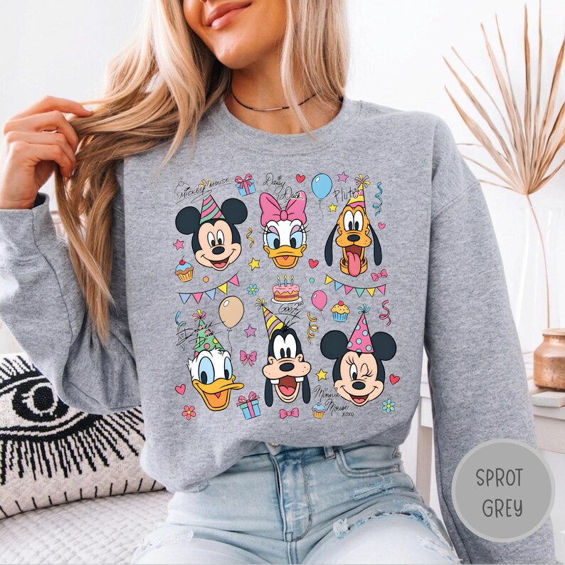 May include: A heather grey crewneck sweatshirt featuring a colourful graphic print of Disney characters including Mickey Mouse, Minnie Mouse, Donald Duck, Daisy Duck, Goofy, and Pluto wearing party hats, surrounded by balloons, cupcakes, and gifts.